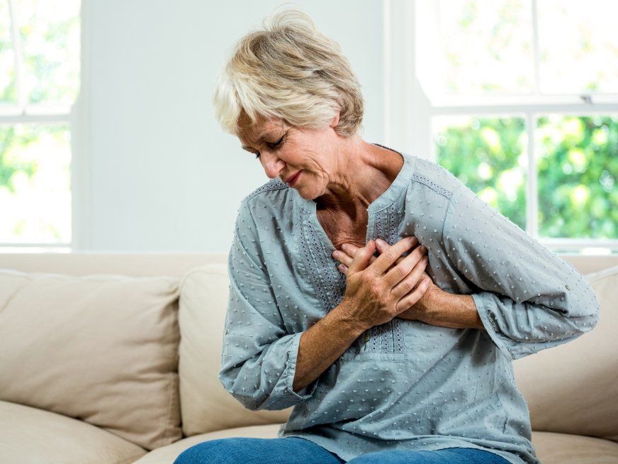 Senior woman suffering from chest pain while sitting on sofa at home