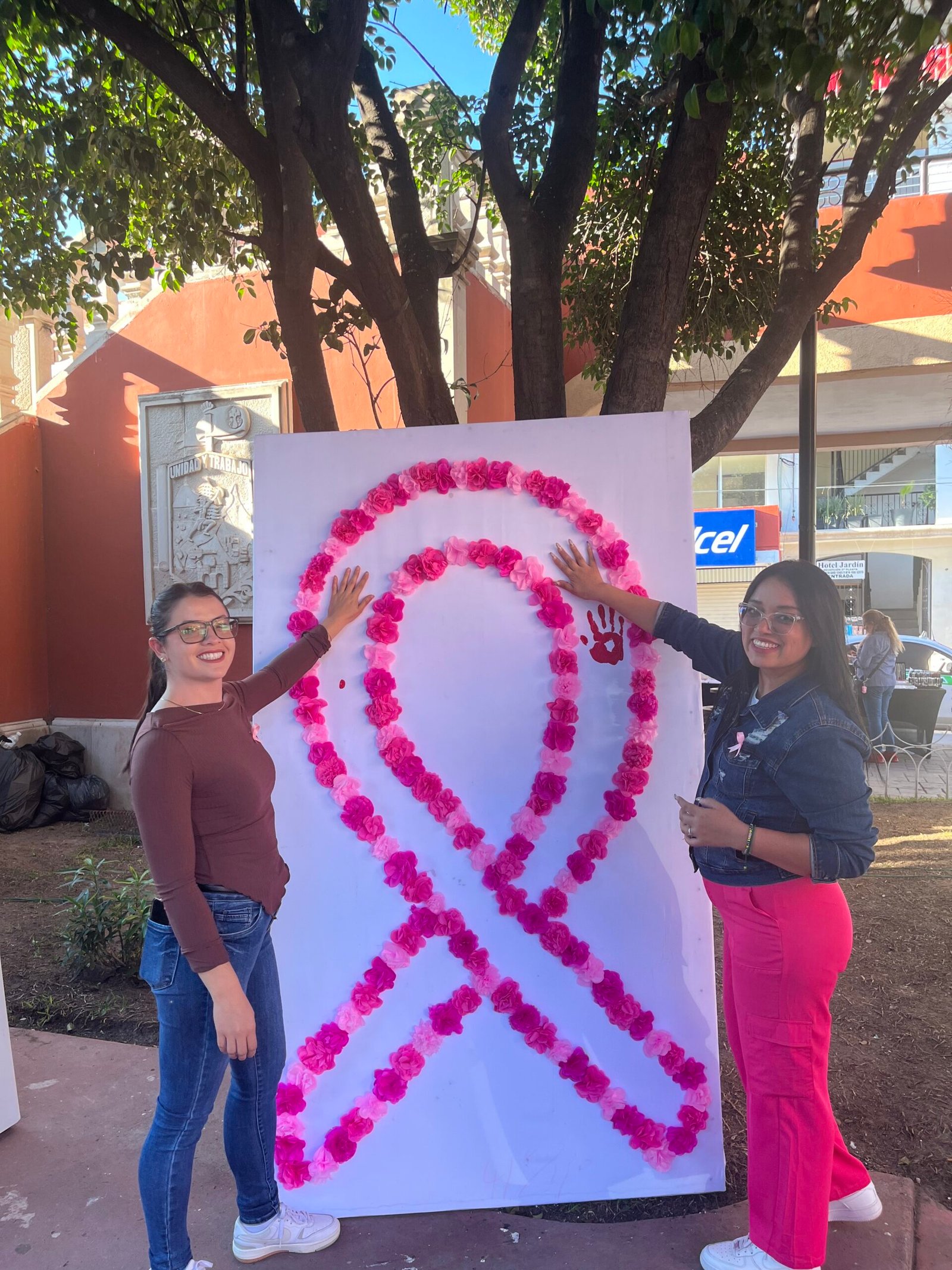 Participantes colocando sus manos sobre un gran moño rosa simbólico.