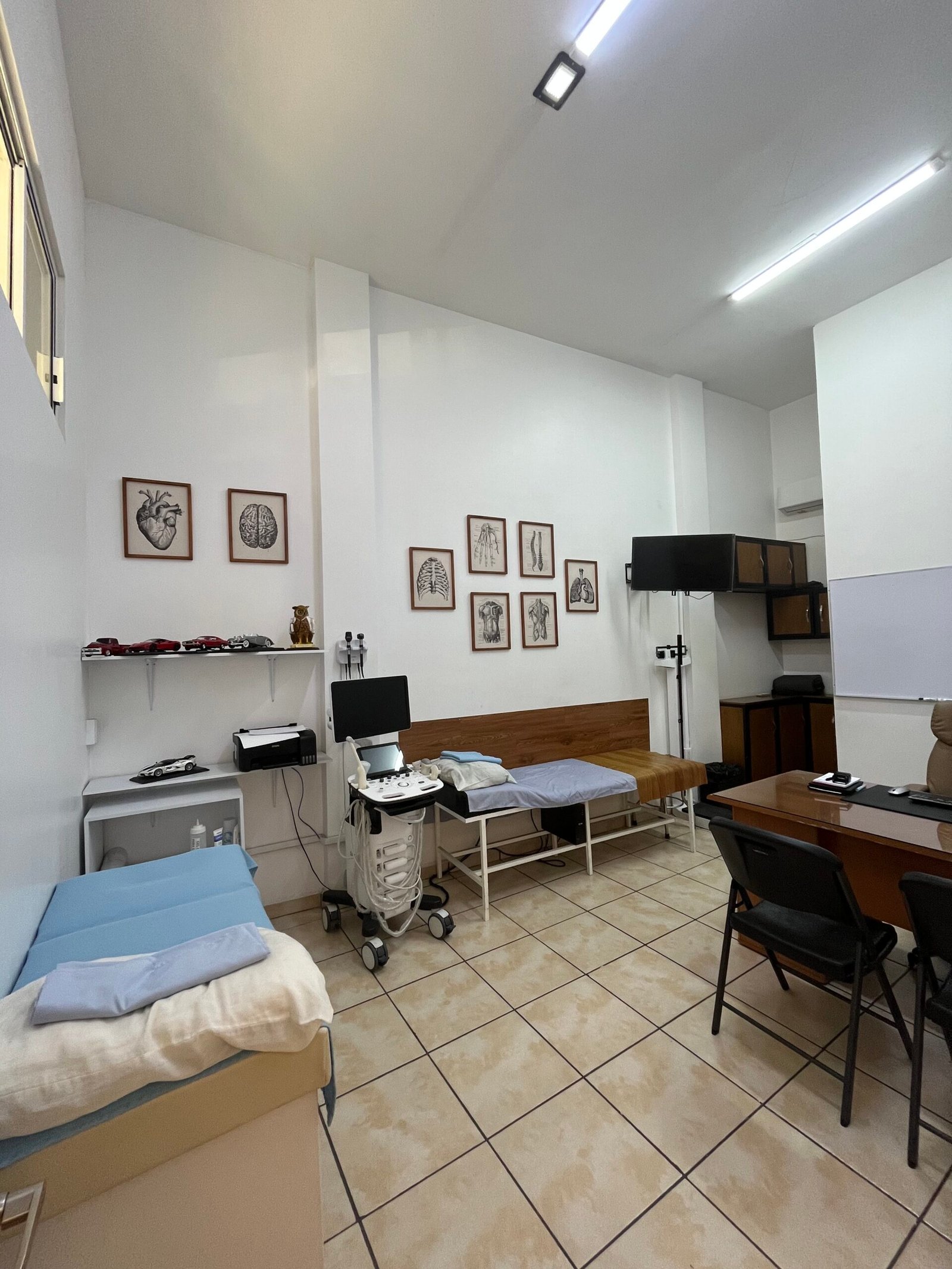 Consultorio médico con equipo de ultrasonido, camilla de exploración y escritorio de atención bajo iluminación clara.